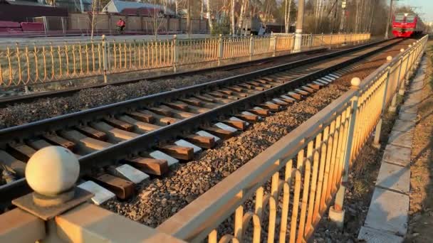 Rusia, San Petersburgo, 25 de abril de 2020: El tren eléctrico de pasajeros de la compañía ferroviaria rusa RZD se acerca a la estación de tren al atardecer, color rojo, el ferrocarril oxidado — Vídeo de stock