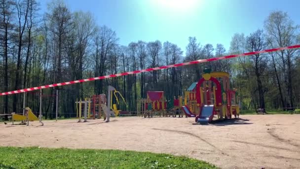 A játszóteret egy piros-fehér szalaggal kerítették be a parkban a karantén alatt a koronavírus világjárvány idején, nincsenek gyerekek a helyszínen, a belépés le van zárva. — Stock videók