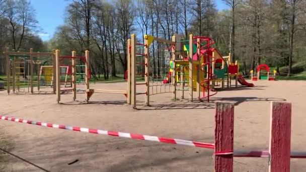 Детская площадка огорожена красно-белой лентой в парке во время карантина во время пандемии коронавируса в мире, детей на месте нет, доступ закрыт — стоковое видео