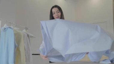 Genç, uzun saçlı esmer kız dikiş atölyesinde terzilik için bir masaya kumaş seriyor, mavi renk, el işi kağıt.