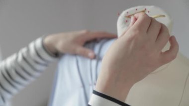 Giysi tasarımcısının yavaş çekim videosu dikiş ajansındaki bir mankenle çalışıyor, 46 beden, mavi kumaşla dikiş ustasının elleri, kırmızı uçlu iğneler dikiyor.