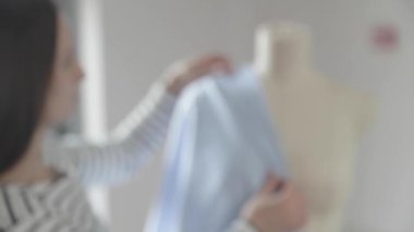 Giysi tasarımcısının yavaş çekim videosu dikiş ajansındaki bir mankenle çalışıyor, 46 beden, mavi kumaşla dikiş ustasının elleri, kırmızı uçlu iğneler dikiyor.