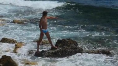 Genç yakışıklı adam kayalıklarda duruyor ve bir deniz dalgası bekliyor, Güney Fransa, Kaptan Dail, gülümsüyor ve eğleniyor, kayalık kıyılarda, su sıçrıyor