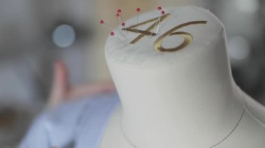 Giysi tasarımcısının yavaş çekim videosu dikiş ajansındaki bir mankenle çalışıyor, 46 beden, mavi kumaşla dikiş ustasının elleri, kırmızı uçlu iğneler dikiyor.