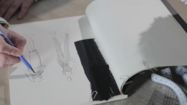 Αργή κίνηση βίντεο του κοριτσιού σχεδιάζει το σκίτσο του μελλοντικού μοντέλου των ρούχων στο σημειωματάριο, εργαλεία για ράψιμο, γραφείο ράψιμο, ένα μάτσο λουλούδια, χάρτινη τέχνη, κορυφαία άποψη — Αρχείο Βίντεο