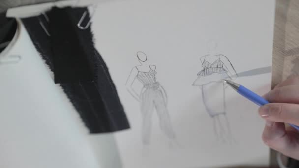 Vidéo au ralenti de la jeune fille dessine le croquis du futur modèle de vêtements dans le carnet, outils pour la couture, agence de couture, un bouquet de fleurs, artisanat en papier, vue de dessus — Video