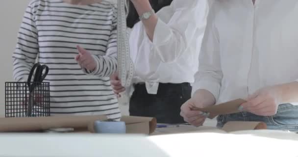 Медленное движение видео модельера, который работает за столом с кривыми и узором, рисует кусочек мыла, вокруг лежит ножницы, сантиметр, ноутбук с эскизом, швейная студия, вид сверху — стоковое видео