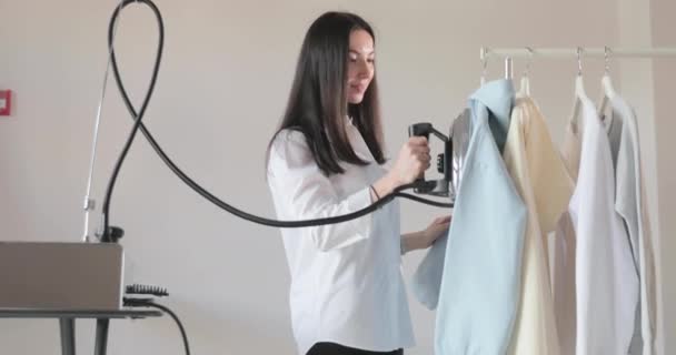 Slow-motion video van de jonge mooie meisje ijzers kleding die hangt op de reling, stoom in verticale situatie, een professionele strijkijzer met stoom, naaien productie, studio, agentschap — Stockvideo