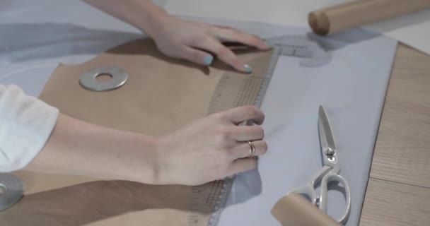 Powolny film z projektantem mody, który pracuje przy stole z krzywiznami i wzorem, rysuje kawałek mydła, wokół leży nożyczki, centymetr, notatnik ze szkicem, studio szycia, widok z góry — Wideo stockowe