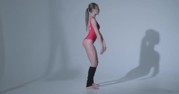 Красивая девушка в красном спортивном костюме и черных леггинсах занимается гимнастикой, купальником, красивой кожей, фигурой, босиком — стоковое видео