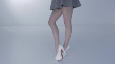 Uzun beyaz topuklu güzel bir kadının uzun bacakları, kırmızı bir ayakkabı tabanı, kısa bir etek, beyaz arka planda ayaklar dans ediyor, coquetler, kısa etek ters dönmüş, spor figürü
