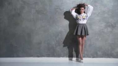 Kıvırcık saçlı, kıvırcık saçlı, kameranın önünde kıvrılıp flört eden, beyaz topuklu, kırmızı bir ayakkabı tabanı, kısa bir etek, gri bir arka plan, farklı duygular...