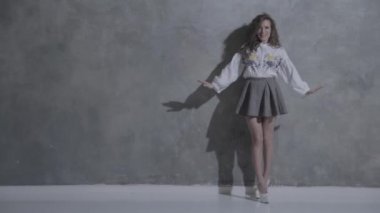 Kıvırcık saçlı, kıvırcık saçlı, kameranın önünde kıvrılıp flört eden, beyaz topuklu, kırmızı bir ayakkabı tabanı, kısa bir etek, gri bir arka plan, farklı duygular...