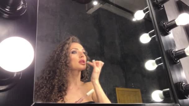 Den unga vackra kvinna med lockigt hår, flickan gör för sig själv makeup, hon slingrar sig och poserar framför spegeln, på gott humör, hon att förbereda sig för en fest, belysning, hon koketter — Stockvideo