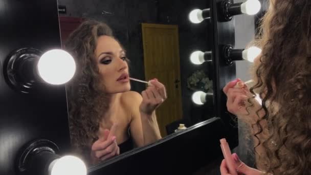 De jonge mooie vrouw met krullend haar, het meisje doet zichzelf make-up, ze kronkelt en poseert voor de spiegel, in goed humeur, ze voor te bereiden op een feest, verlichting, ze coquets — Stockvideo