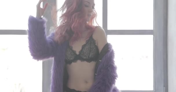 The young beautiful girl with long curly red hair in a violet fur coat and black underwear poses, flirts and touches hair, Beautiful hips, a sexual figure, a languishing look, ginger hair — Stock Video
