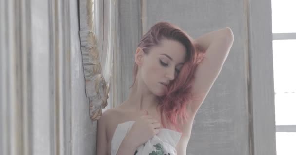 The young beautiful girl with long curly red hair, she is naked, she is covered with a white shirt, she poses, flirts and touches hair, beautiful hips, a sexual figure, a languishing look, ginger hair — Stock Video