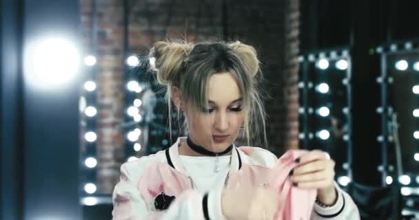 Het tienermeisje in een wit t-shirt poseert voor de spiegel in een make-upkamer, danst, flirt, kronkelt, een haarjurk in de vorm van trossen, een choker in de nek, armbanden aan de handen — Stockvideo