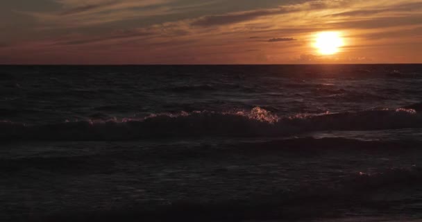 Sandkusten med en tidvattenvåg vid solnedgången, stenar, sand, vågor, ingen, landskap, lugn och ro, solen faller, stänk, reflektioner av sol på vatten — Stockvideo