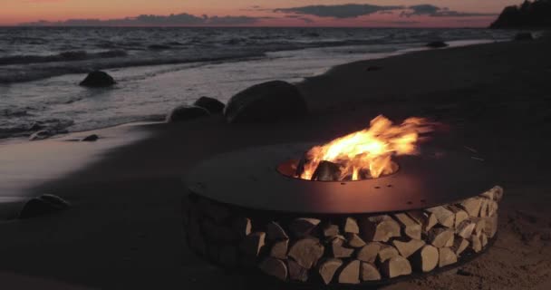 A paisagem do belo metal em volta de uma lareira na costa arenosa com uma onda de maré ao pôr do sol, pedras, tranquilidade, o sol cai, lenha, carvões vermelhos, ninguém — Vídeo de Stock