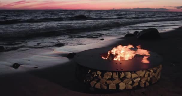 El paisaje del metal hermoso alrededor de una chimenea en la costa arenosa con un maremoto al atardecer, piedras, tranquilidad, el sol cae, leña, carbones rojos, nadie — Vídeos de Stock