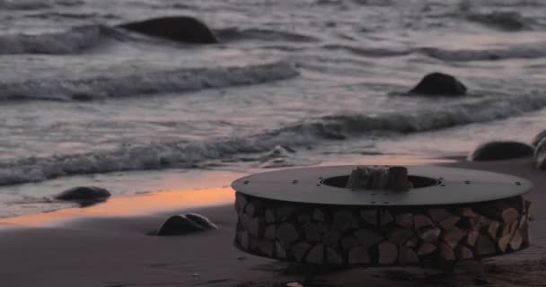 A paisagem do belo metal em volta de uma lareira na costa arenosa com uma onda de maré ao pôr do sol, pedras, tranquilidade, o sol cai, lenha, carvões vermelhos, ninguém — Vídeo de Stock