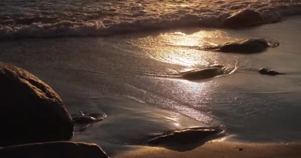 La costa arenosa con el maremoto al atardecer, las piedras, la arena, las olas, nadie, el paisaje, la tranquilidad, el sol cae, las salpicaduras, los reflejos del sol sobre el agua — Vídeos de Stock