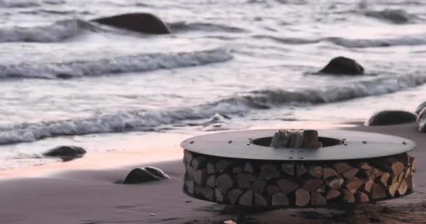 A paisagem do belo metal em volta de uma lareira na costa arenosa com uma onda de maré ao pôr do sol, pedras, tranquilidade, o sol cai, lenha, carvões vermelhos, ninguém — Vídeo de Stock