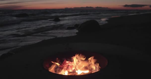 Het landschap van het prachtige metaal rond een open haard aan de zandkust met een vloedgolf bij zonsondergang, stenen, rust, de zon valt, brandhout, rode kolen, niemand — Stockvideo