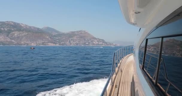 Медленное движение яхты идет с большой скоростью, пенная дорожка от яхты, роскошная жизнь, ясная солнечная погода, Лигурийское море, горы на заднем плане — стоковое видео