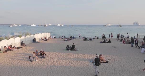França, Cannes, 27 de maio de 2017: Praia de Cannes durante o cinema Festival de Cannes ao pôr-do-sol, cafés de praia, guarda-chuvas, céu rosa, iates de luxo no horizonte — Vídeo de Stock