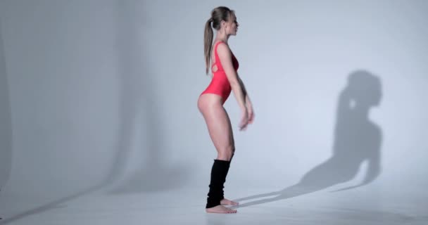 Bella ragazza in un abito sportivo rosso e leggings neri è impegnata in ginnastica, costume da bagno, bella pelle, figura, a piedi nudi — Video Stock