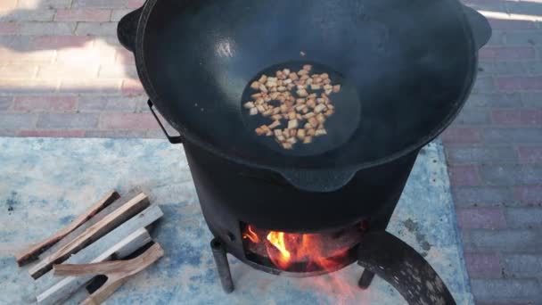 El tostado de la grasa de cordero hasta el estado de las galletas, alguna etapa de la preparación del plato nacional uzbeko pilaf, la pala para la comida, el caldero, el fuego, la leña, el aire libre — Vídeos de Stock