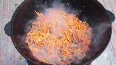 Ulusal Özbek tabak pilavı, pilav, plov, büyük tavada etli havuç hazırlama. Pişirme işlemi, ateş açın. Kazanda ateşte yemek pişirmek. Kaymağını yavaşça karıştır. Küçük kesilmiş havuç ilavesi