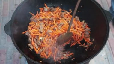 Ulusal Özbek tabak pilavı, pilav, plov, büyük tavada etli havuç hazırlama. Pişirme işlemi, ateş açın. Kazanda ateşte yemek pişirmek. Kaymağını yavaşça karıştır. Küçük kesilmiş havuç ilavesi