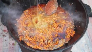 Ulusal Özbek tabak pilavı, pilav, plov, büyük tavada etli havuç hazırlama. Su ekle, pişirme işlemi, ateş aç. Kazanda ateşte yemek pişirmek. Kaymağını yavaşça karıştır. Baharat ekle