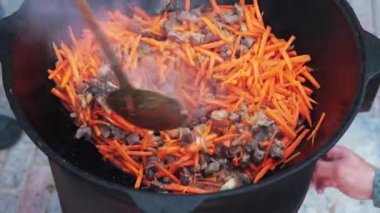 Ulusal Özbek tabak pilavı, pilav, plov, büyük tavada etli havuç hazırlama. Pişirme işlemi, ateş açın. Kazanda ateşte yemek pişirmek. Kaymağını yavaşça karıştır. Küçük kesilmiş havuç ilavesi