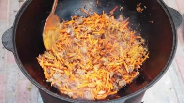 Ulusal Özbek tabak pilavı, pilav, plov, büyük tavada etli havuç hazırlama. Pişirme işlemi, ateş açın. Kazanda ateşte yemek pişirmek. Kaymağını yavaşça karıştır. Baharat ekle