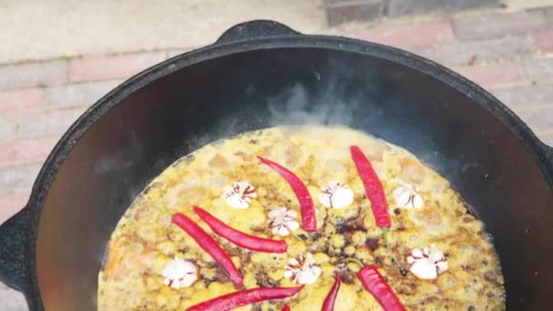 Plato nacional uzbeko pilaf, pilaw, plov, arroz con carne en sartén grande. Llevar a ebullición, proceso de cocción en un caldero en el fuego, pimiento rojo y todo el ajo — Vídeos de Stock