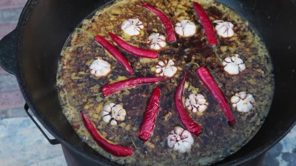 Prato uzbeque nacional pilaf, pilaw, plov, arroz com carne em grande panela. Processo de cozinha em um caldeirão em chamas. Adicione uma pimenta vermelha e alho — Vídeo de Stock