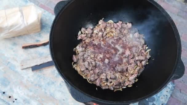 Národní uzbecký pilaf, pilaf, plov, cibule a maso ve velké pánvi. Vaření, zahajte palbu. Vaření v kotli v plamenech. Pomalu zamíchejte kluzákem. Přidat maso berana a trochu se opéká — Stock video