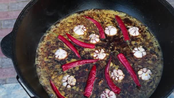 Plato nacional uzbeko pilaf, pilaw, plov, arroz con carne en sartén grande. Proceso de cocción en un caldero en llamas. Añadir un pimiento rojo y ajo — Vídeo de stock