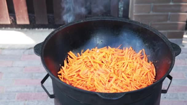 Preparazione di piatto uzbeko nazionale pilaf, pilaw, plov, carota con carne in pentola grande. Processo di cottura, fuoco aperto. Cucinare in un calderone in fiamme. Mescolare lentamente con uno schiumatoio. Aggiunta di piccole carote tagliate — Video Stock