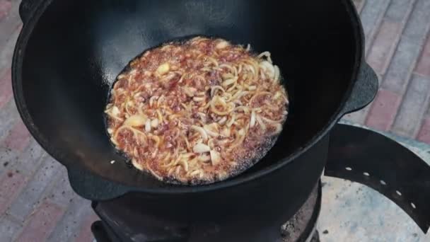 National Uzbek dish pilaf, pilaw, plov, rice with meat in big pan. Cooking process, open fire. Cooking in a cauldron on fire. Preparation stages. Onions roasting to color of caramel, pilau — Stock Video