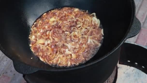 Prato uzbeque nacional pilaf, pilaw, plov, arroz com carne em grande panela. Processo de cozedura, fogo aberto. Cozinhar num caldeirão a arder. Estágios de preparação. Cebolas assando à cor de caramelo, pilau — Vídeo de Stock