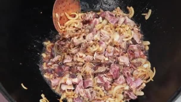 乌孜别克族菜卷、毛皮、杂烩、洋葱和肉在大锅里.烹饪过程，开火。在烧着的大锅里做饭。用撇子慢慢搅拌.加羊肉和一点烤肉 — 图库视频影像
