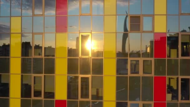 El edificio de oficinas con vidrieras multicolores al atardecer, filmación de video por un dron, reflejo del sol en una ventana, paisaje urbano — Vídeo de stock