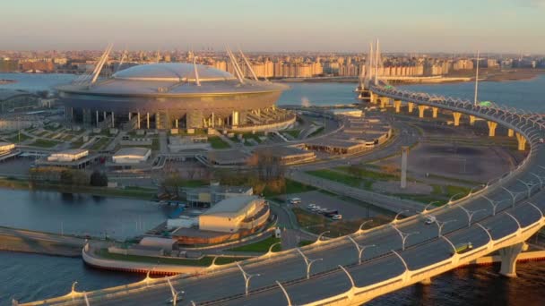 Oroszország, Szentpétervár, 2020. május 06.: Légi felvétel a Gazprom aréna stadionjáról naplementekor, autópálya és kábelhíd, nyugati nagy sebességű átmérő, éjszakai megvilágítás bekapcsolva, rózsaszín ég — Stock videók