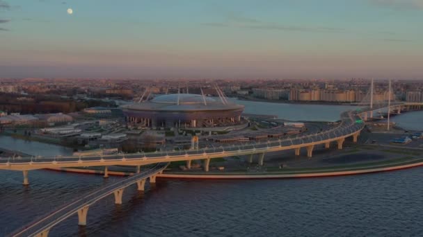 Rusko, Petrohrad, 6. května 2020: Letecké video stadionu Gazprom arény při západu slunce, dálnice a lanovka, západní vysokorychlostní průměr, noční osvětlení zapnuto, růžová obloha — Stock video
