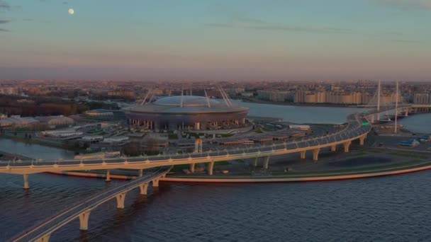 Russia, St.Petersburg, 2020 년 5 월 6 일 : Aerial video of Gazprom arena Stadium at sunset, highway and cable bridge, Western high-speed diameter, night lights is on, pink sky — 비디오